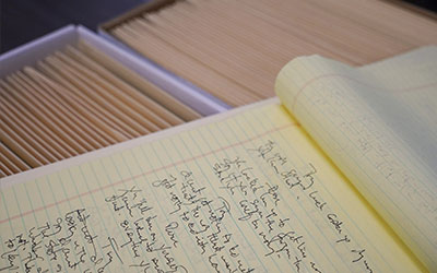 A notebooks with hand written information on top of two boxes of files.